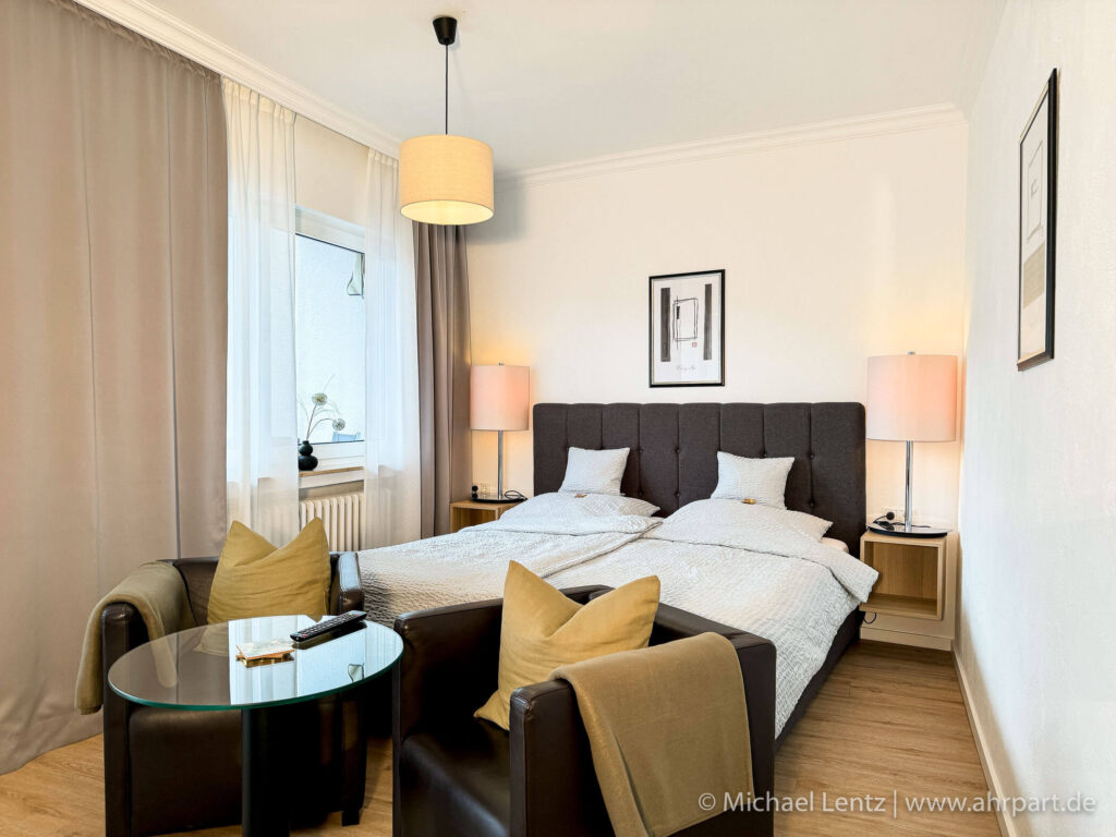 Großes Doppelbett eines Komfort Doppelzimmer im AHRPART Hotel. Auf den gemütlichen Sesseln kann man abends ein leckeres Glas Ahrwein trinken. Hier wachsen sie morgens mit Blick auf die Ahr und das Kurhaus auf.